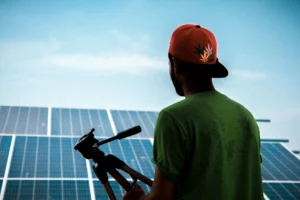 pexels-alimadad-1254997_optimized - RenovSmart Homme de dos tenant un trépied devant des panneaux solaires photovoltaïques sous un ciel bleu.