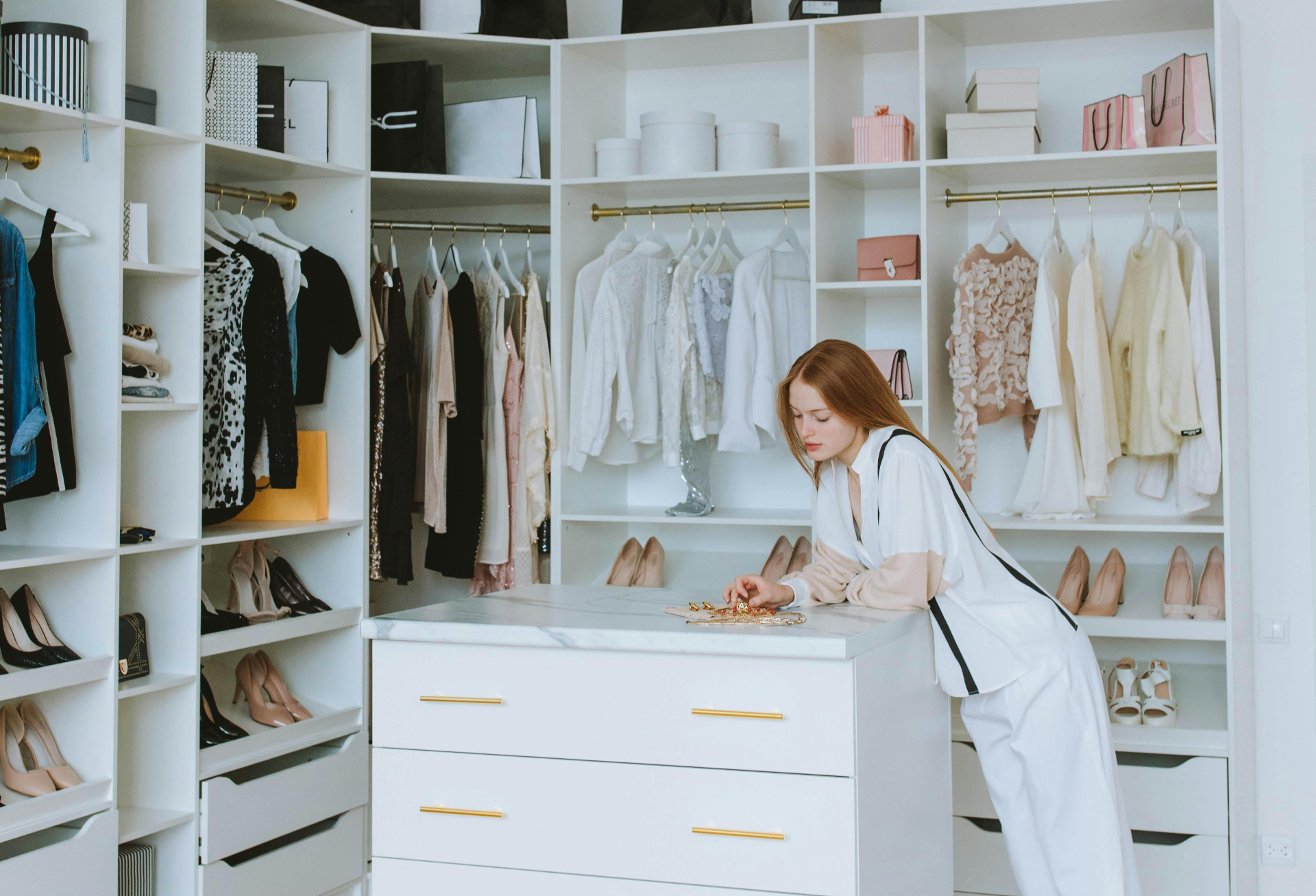 Jeune femme dans un dressing lumineux et bien organisé, regardant des bijoux posés sur un îlot central.