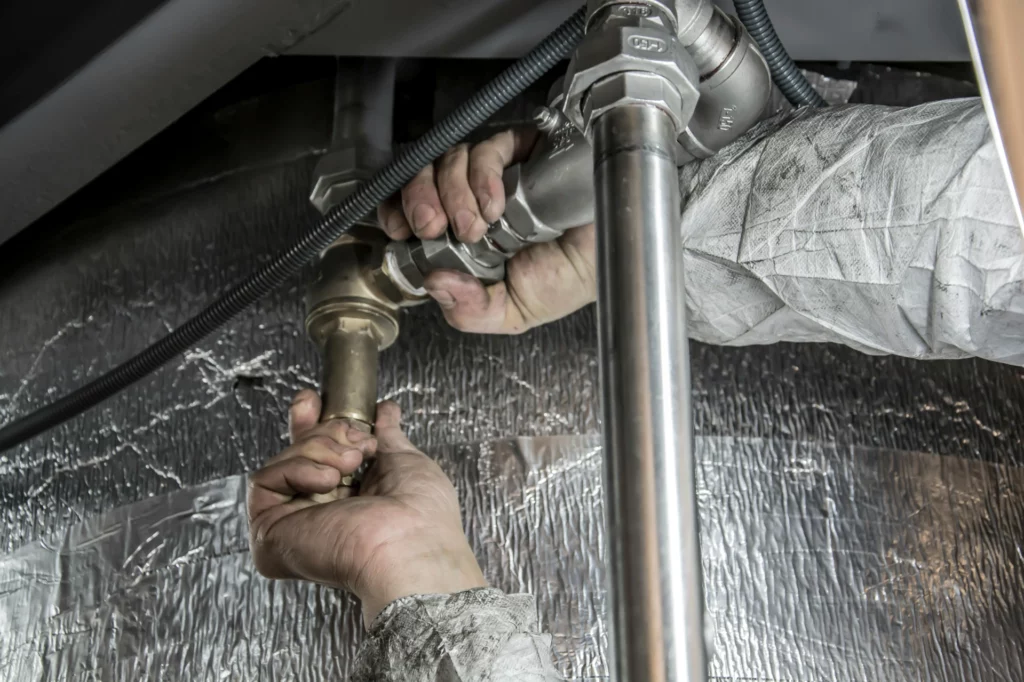 pexels-anilkarakaya-6419128_optimized - RenovSmart Plombier ajustant un raccord de tuyauterie en métal dans un espace technique.