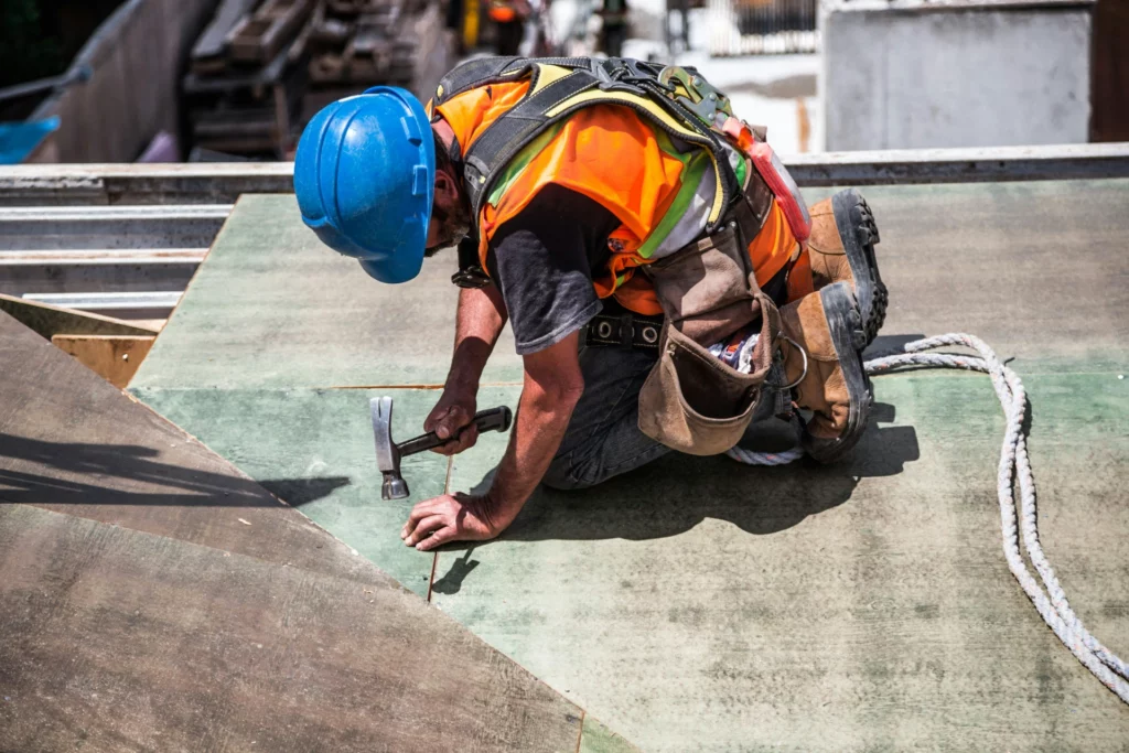 pexels-burst-544966 1_optimized - RenovSmart Ouvrier du bâtiment en casque bleu et gilet orange clouant une planche en bois sur un chantier.