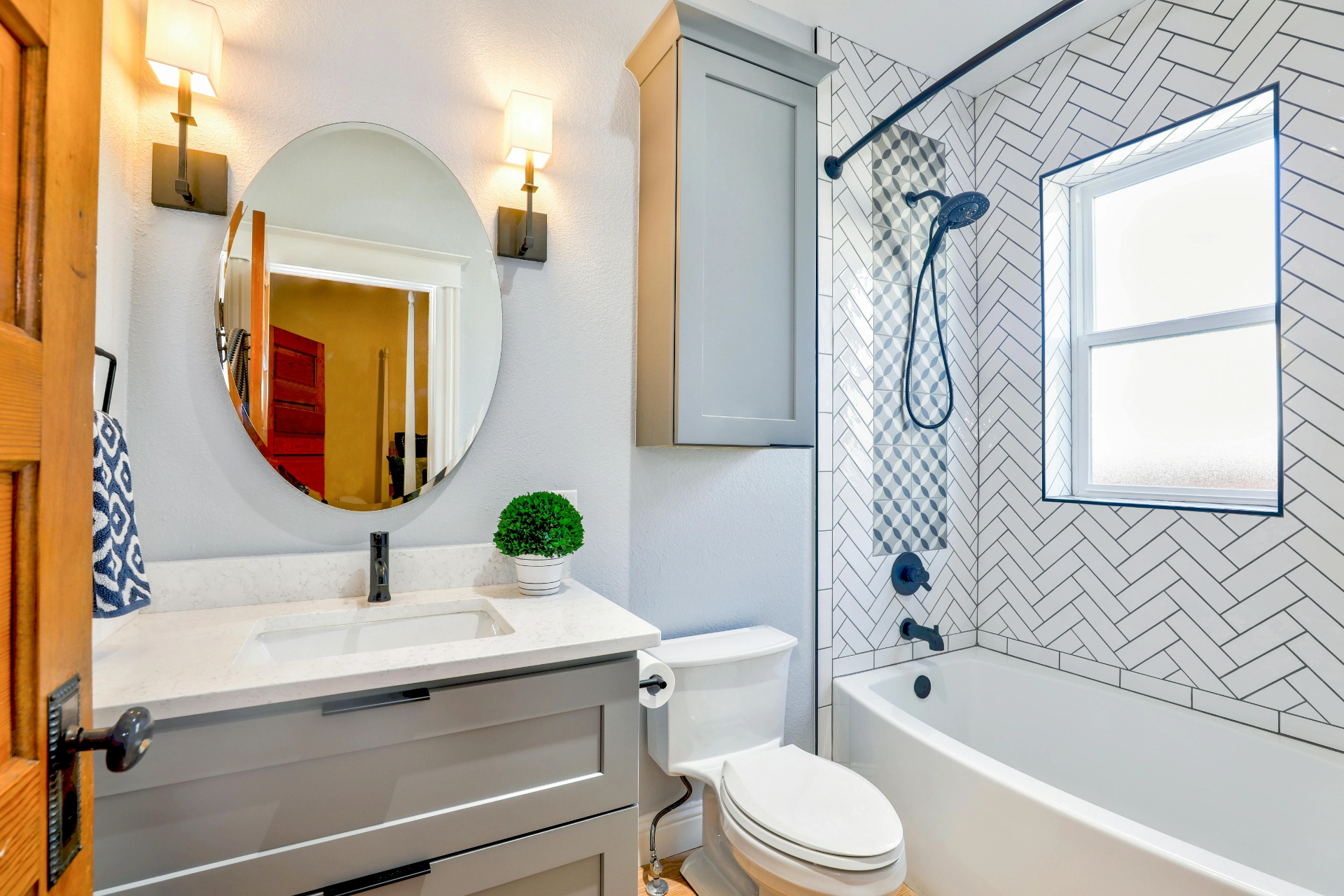 Salle de bain moderne avec lavabo, miroir rond, baignoire, douche à effet pluie et carrelage blanc à motif.