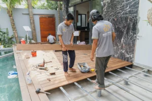 pexels-cong-ty-cp-thi-cong-m-c-phat-2533691-4135926_optimized - RenovSmart Deux ouvriers posant des lames de terrasse en bois composite dans un jardin moderne avec piscine.