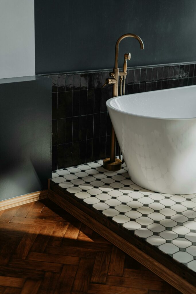 Baignoire îlot blanche sur carrelage hexagonal avec robinetterie dorée dans une salle de bain moderne.