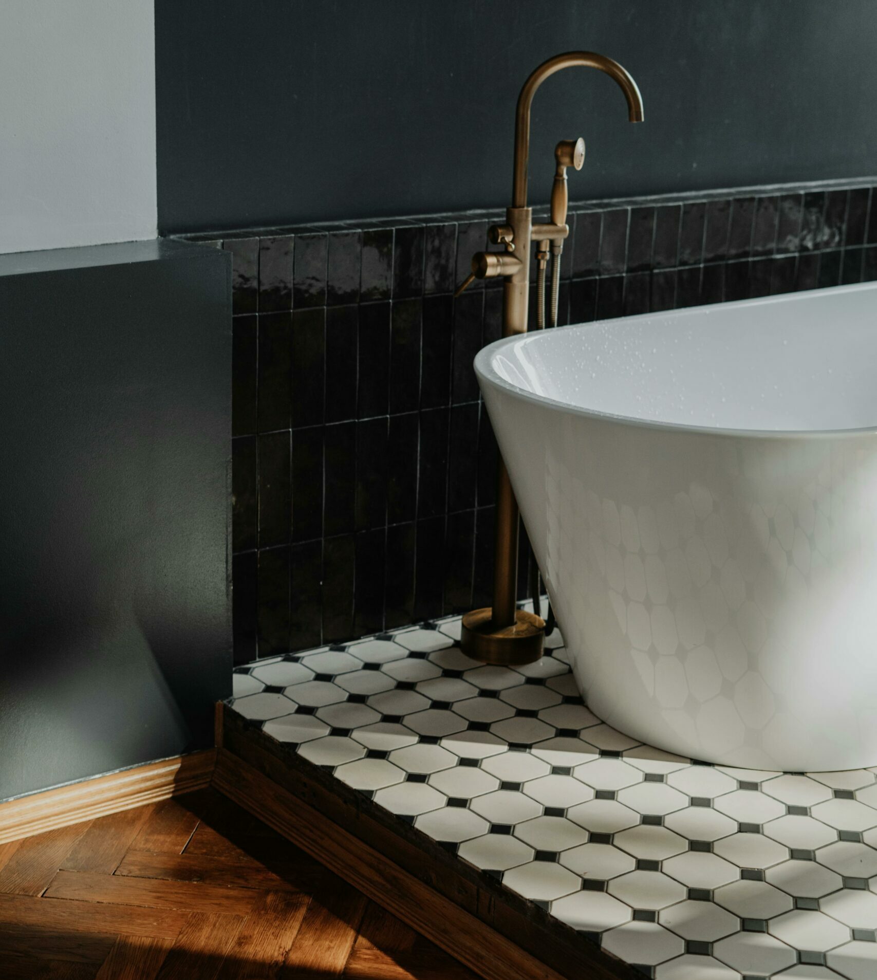 Baignoire îlot blanche sur carrelage hexagonal avec robinetterie dorée dans une salle de bain moderne.