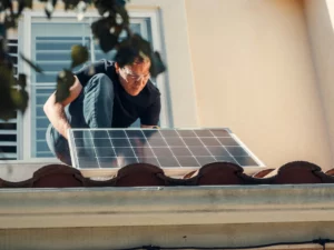 pexels-kindelmedia-9875405_optimized - RenovSmart Homme installant un panneau solaire photovoltaïque sur une toiture en tuiles.