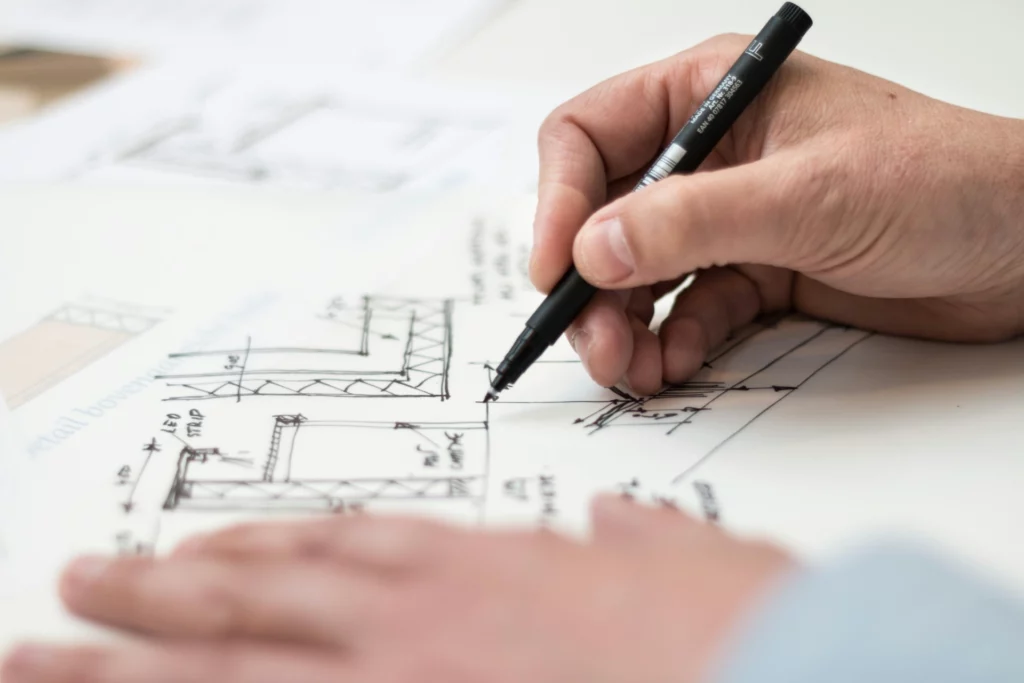 pexels-lexovertoom-1109541_optimized - RenovSmart Main dessinant un plan architectural technique au stylo noir sur une feuille blanche.