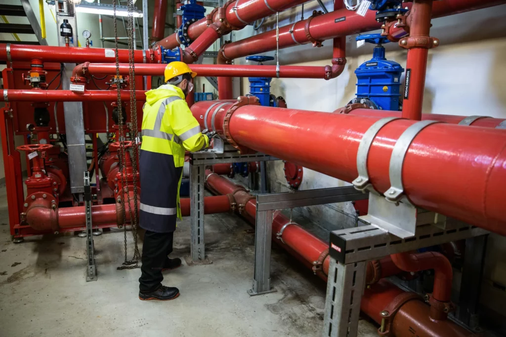 pexels-marianna-zuzanna-498248397-16442684_optimized - RenovSmart Technicien en plomberie industrielle inspectant des grandes canalisations rouges dans une installation technique.