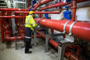 Technicien en plomberie industrielle inspectant des grandes canalisations rouges dans une installation technique.