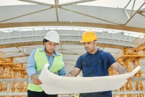 Deux professionnels du bâtiment en chantier examinant des plans de rénovation énergétique.