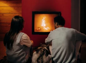 pexels-mikhail-nilov-6530544_optimized - RenovSmart Un couple assis devant une cheminée moderne avec un chien, profitant de la chaleur d’un feu.
