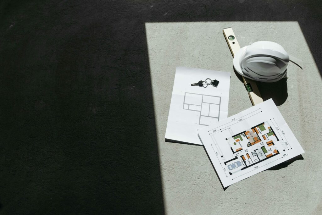Plan architectural avec casque de chantier, niveau à bulle et clés sur fond en béton.