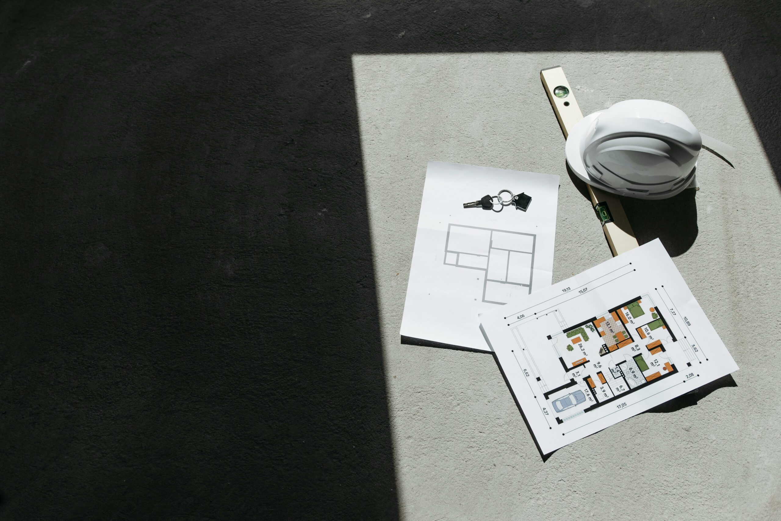 Outils et plans pour un projet de rénovation en Wallonie - RenovSmart Plan architectural avec casque de chantier, niveau à bulle et clés sur fond en béton.