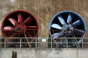 pexels-pixabay-416423_optimized - RenovSmart Deux grandes turbines industrielles, l’une rouge et l’autre bleue, installées sur un mur extérieur avec une grille de protection métallique.