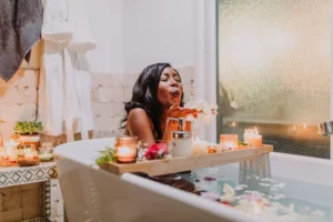 emme soufflant des pétales de fleurs dans une baignoire entourée de bougies allumées.