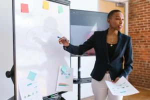 pexels-rdne-7414273_optimized - RenovSmart Femme en réunion expliquant un plan de budget sur un tableau blanc avec des graphiques.