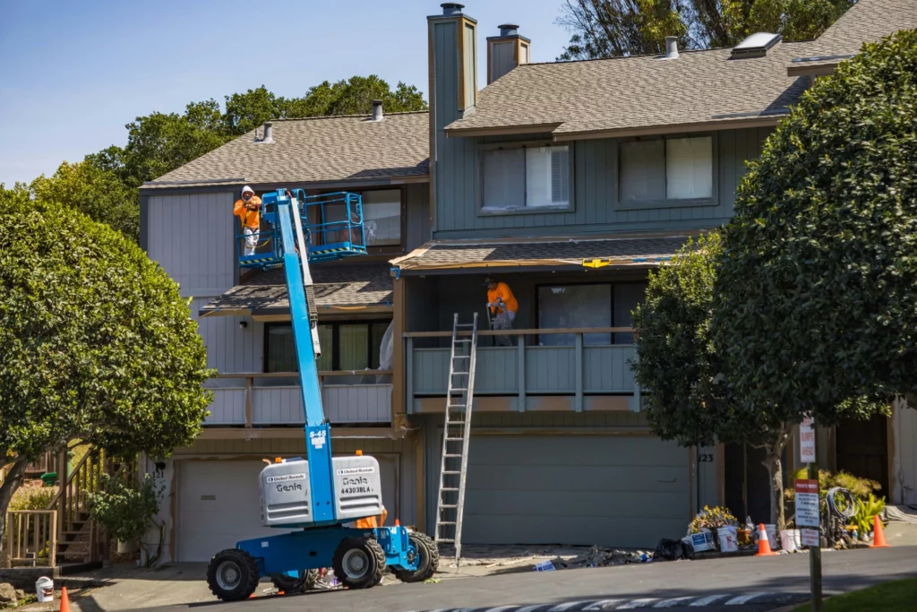 pexels-robertkso-11953905_optimized - RenovSmart Travailleurs en train de rénover la façade d’une maison avec une nacelle élévatrice et une échelle.
