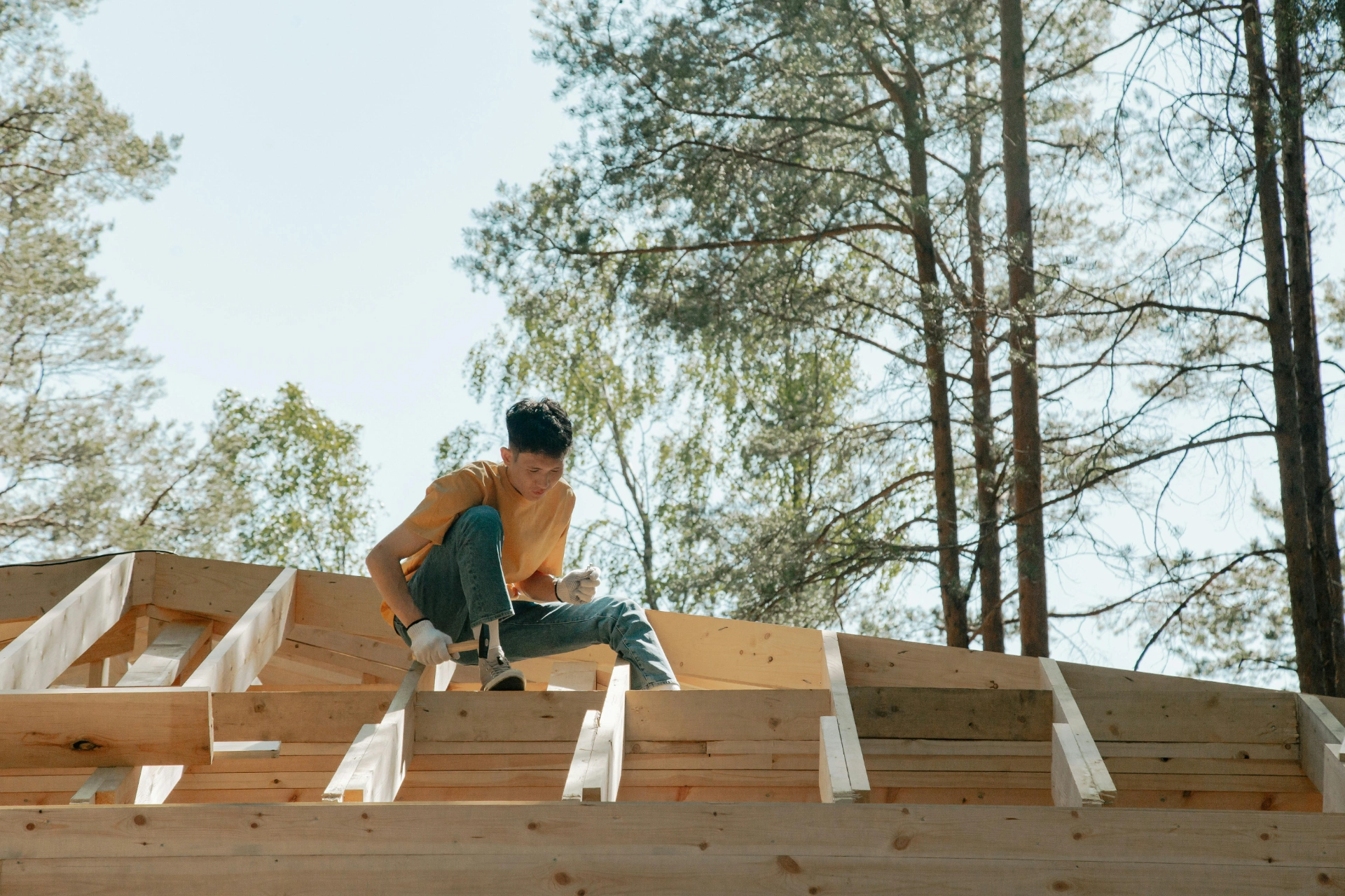 Jeune charpentier travaillant sur une structure en bois en extérieur dans un environnement boisé.