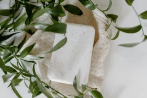 Savon blanc naturel posé sur une éponge en fibre naturelle, entouré de feuilles vertes.