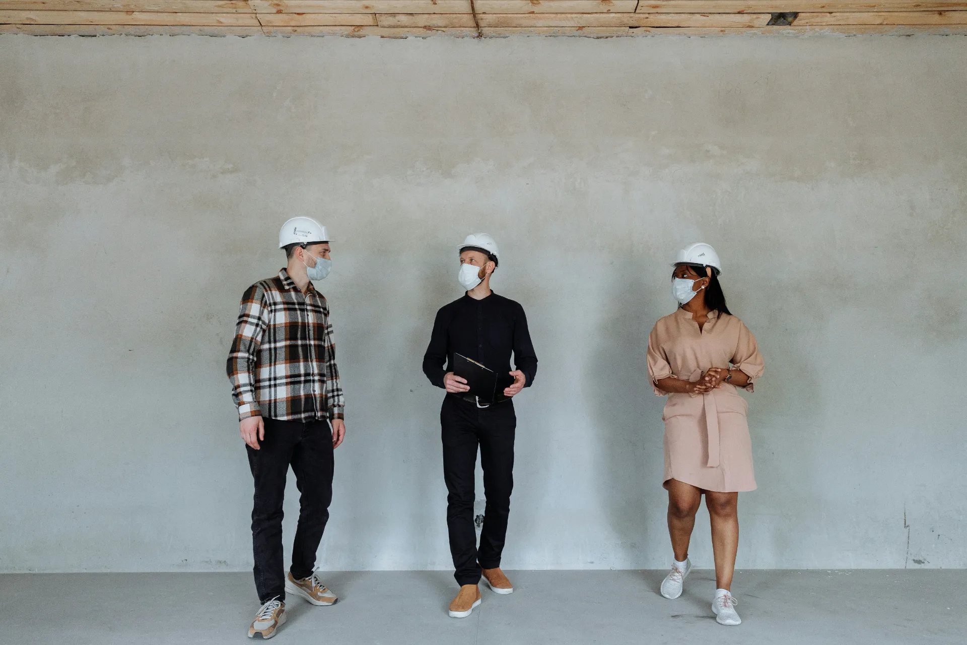 Trois professionnels du bâtiment portant casques et masques discutent sur un chantier intérieur