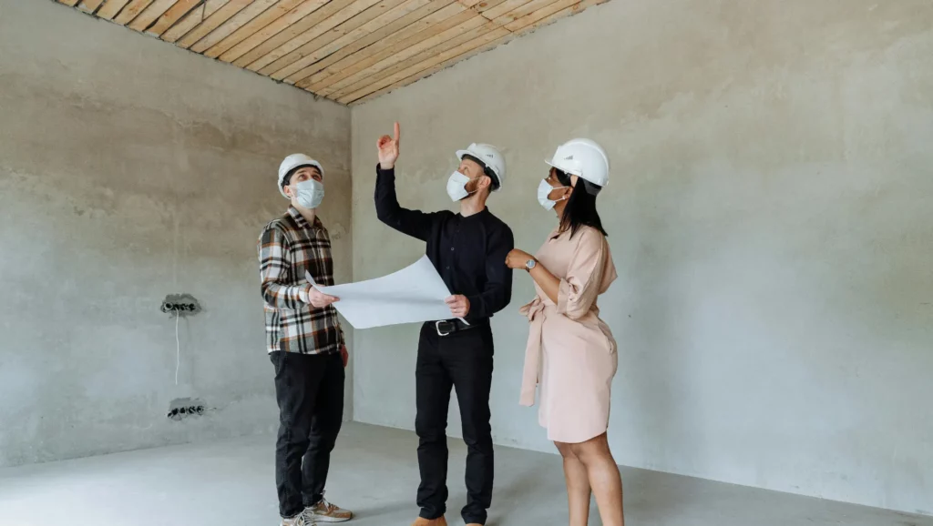 Trois professionnels en casque de sécurité discutent d’un plan dans une pièce en rénovation