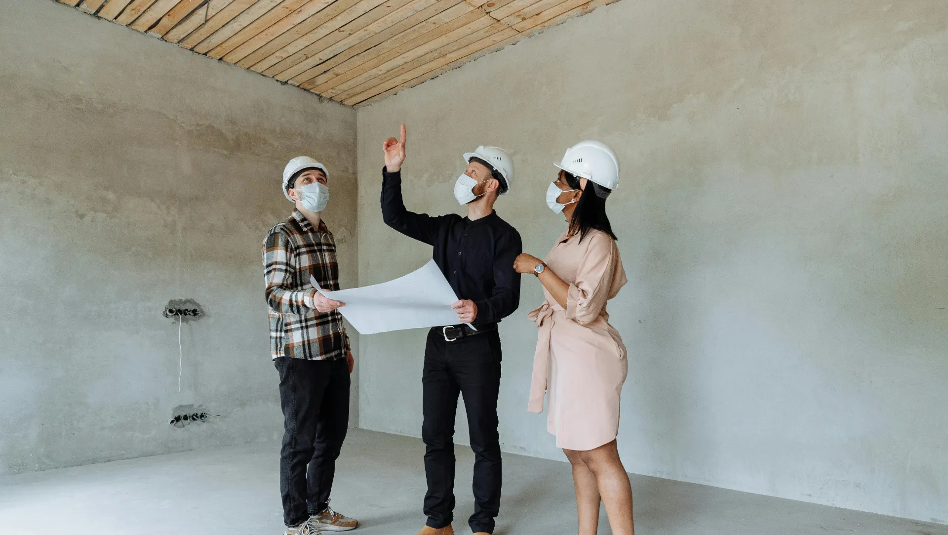 Trois professionnels en casque de sécurité discutent d’un plan dans une pièce en rénovation