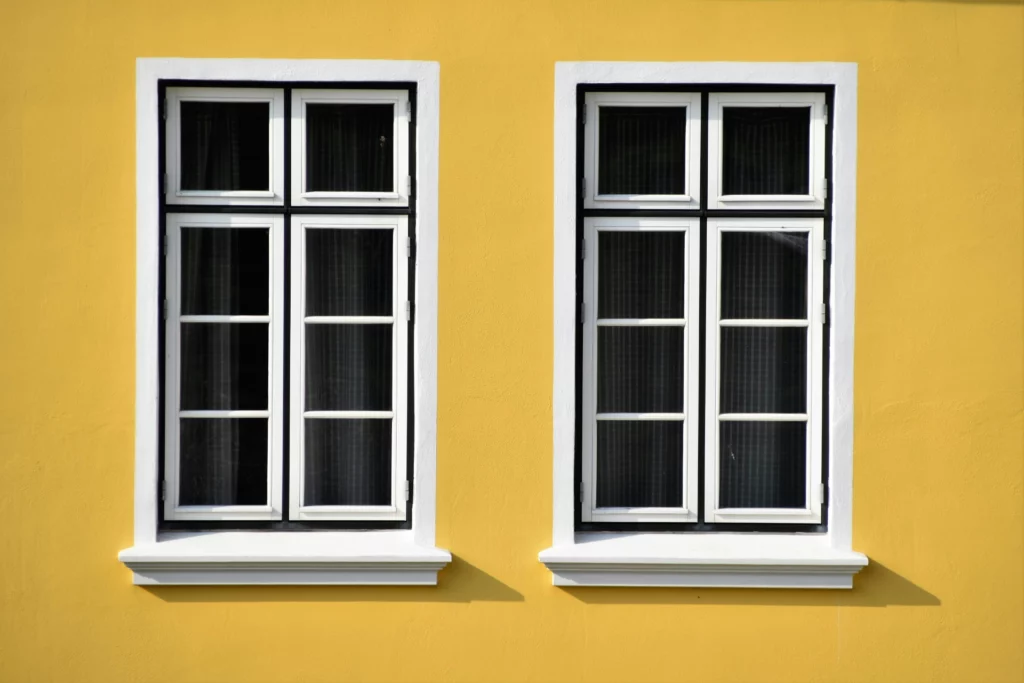 Deux fenêtres blanches à petits carreaux sur un mur jaune vif.