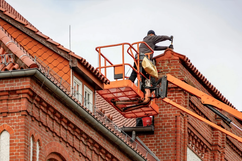 Un ouvrier travaillant sur le toit d'un bâtiment à l'aide d'une nacelle élévatrice orange.
