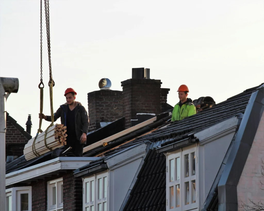 Deux ouvriers sur un toit reçoivent des matériaux à l'aide d'une grue pour des travaux de toiture.