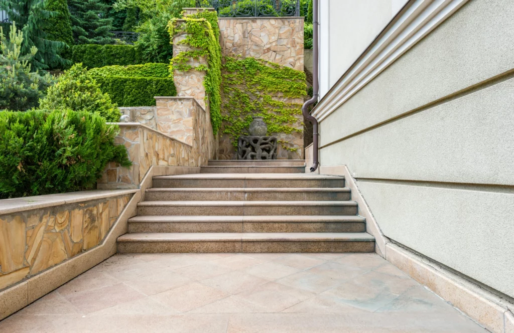 Escaliers extérieurs avec sculpture et végétation. - RenovSmart Escaliers extérieurs en pierre menant à un jardin avec des plantes grimpantes et une sculpture décorative.
