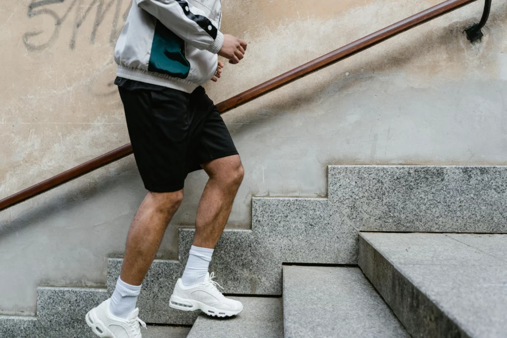 Homme montant les escaliers en tenue sportive. - RenovSmart Un homme montant des escaliers en portant un short noir, des baskets blanches et une veste légère.