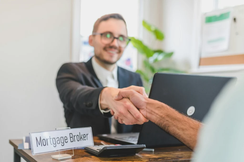 Rencontre avec un courtier en hypothèques - RenovSmart Un courtier en hypothèques serre la main d'un client dans son bureau, souriant et professionnel.