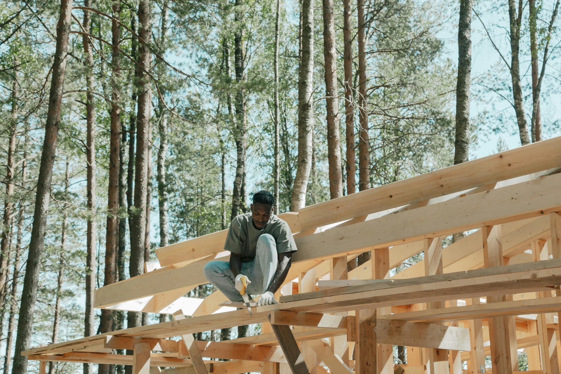 Un ouvrier sur un toit en construction, travaillant avec des outils en bois dans une forêt.

