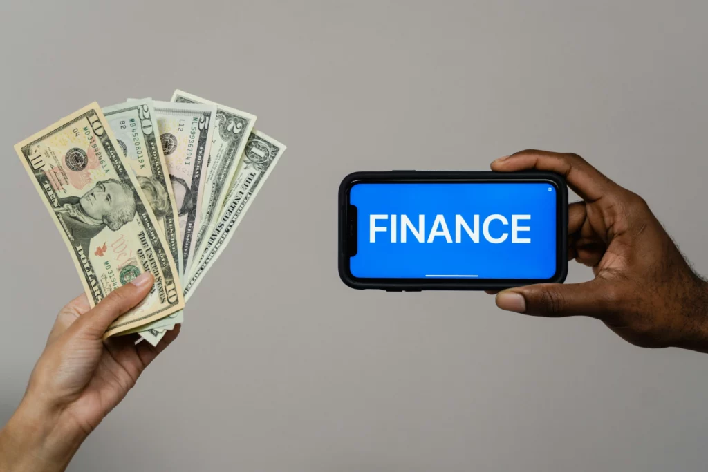 Gestion financière : argent et technologie - RenovSmart Une main tenant des billets de banque et une autre main tenant un smartphone affichant le mot "FINANCE".