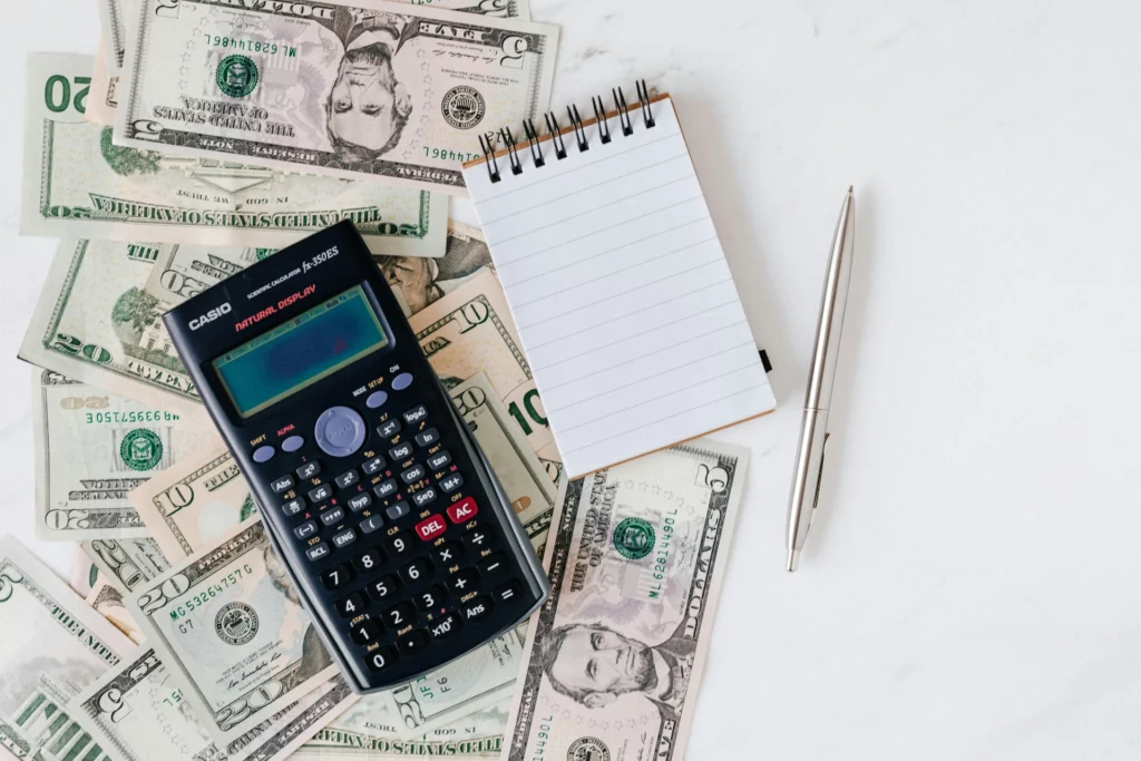 Outils financiers : calculatrice, carnet et billets de banque - RenovSmart Calculatrice, carnet de notes et stylo entourés de billets de banque en dollars.