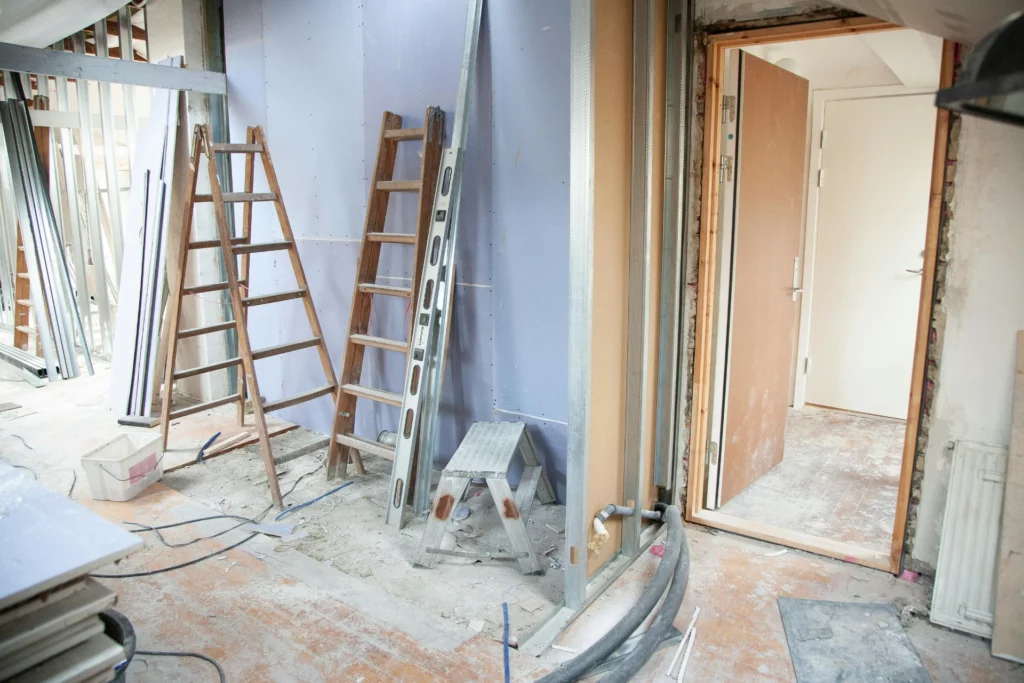 Pièce en cours de rénovation avec échelles, plaques de plâtre et matériel de construction.