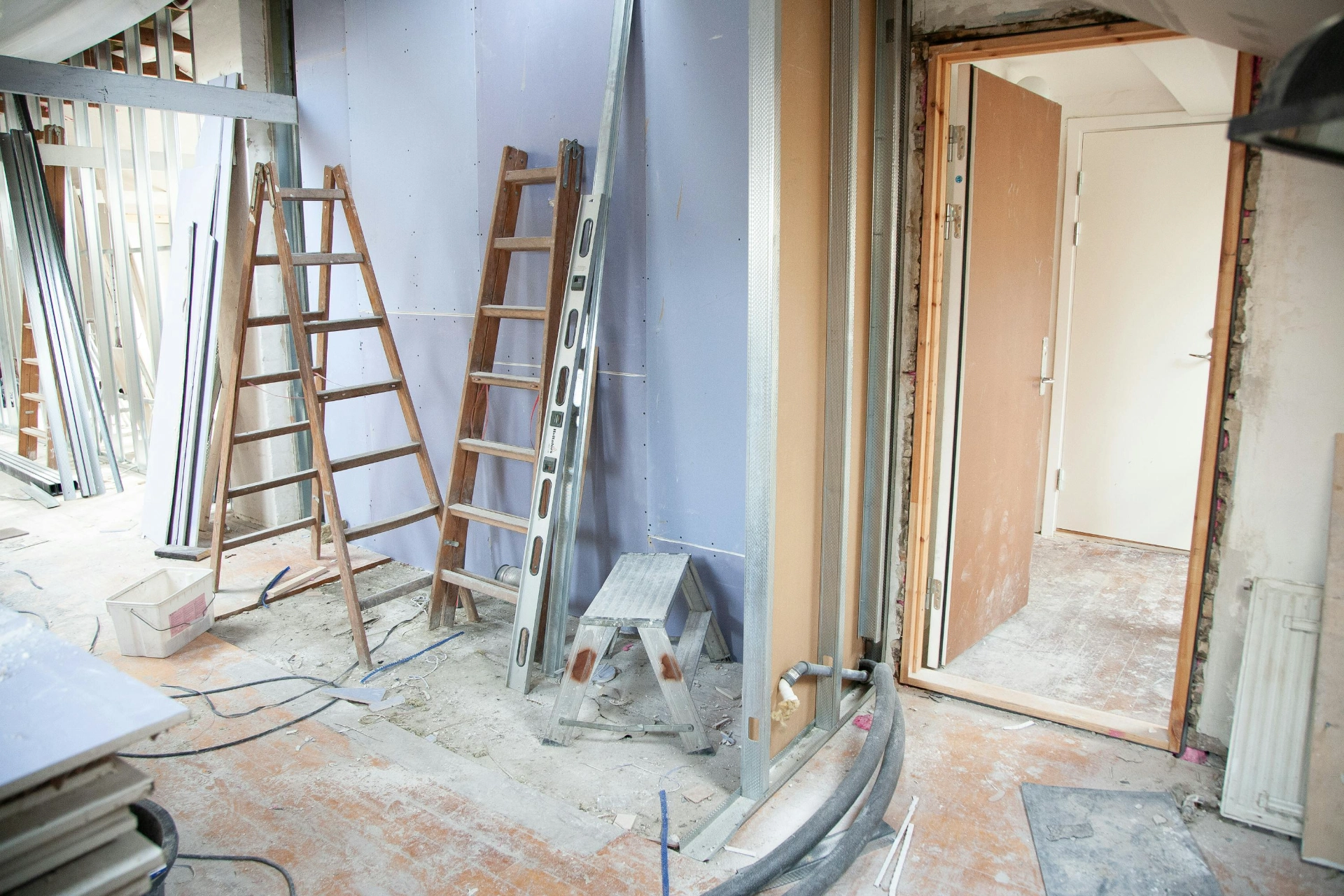 Pièce en cours de rénovation avec échelles, plaques de plâtre et matériel de construction.