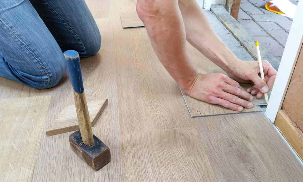 Personne posant un revêtement de sol en bois à l'aide d'outils de bricolage.