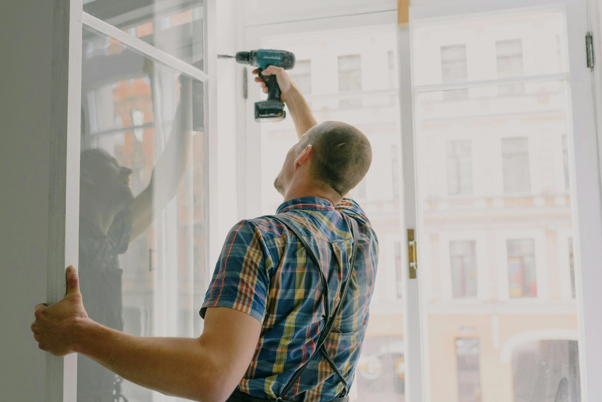 Ouvrier installant une fenêtre avec une visseuse électrique dans un logement en rénovation.